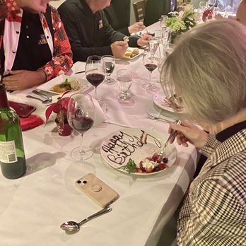 Peacock Cafe - Bday dessert - A woman with blonde hair and glasses is serving herself a dessert on a decorated plate that says 'Happy Birthday' at a dinner gathering. - Wine Bars Near Me - Washington, DC, District of Columbia