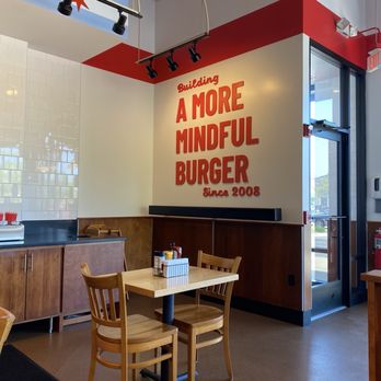 Epic Burger - A dining area inside a burger restaurant features a wooden table with two chairs, a wall sign, and a door leading outside. - Burgers Near Me - Barrington, Illinois