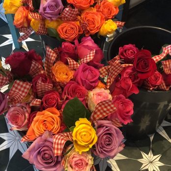 Cedar - Roses for the ladies at Sunday brunch - The image shows several bouquets of roses in different colors such as yellow, orange, pink, purple, and red. The roses are decorated with red and white checkered ribbons and are arranged on a patterned black and white tiled floor. Some bouquets are placed in black containers, and the flowers are displayed in a way that highlights their vibrant colors and decorative ribbons. - Breakfast & Brunch Near Me - Covington, Kentucky