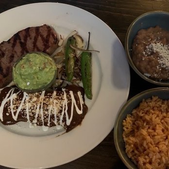 Amuleto Mexican Table - Carne Asada - A meal featuring grilled steak, guacamole, and vegetables on a white plate, accompanied by bowls of rice and beans. - Mexican Near Me - Waltham, Massachusetts