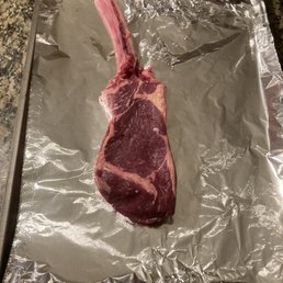 Tomahawk! - A raw, bone-in cut of red meat, possibly a steak, is laid on aluminum foil on a baking sheet, ready for cooking or preparation.