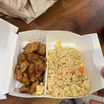 Panda Express - Kids meal number 2 - A white takeout box holds fried chicken pieces coated in sauce and fried rice with small vegetable pieces, placed on a wooden table. - Chinese Near Me - Mclean, Virginia