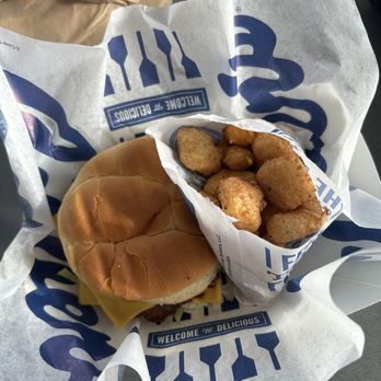 Culver's - A fast food meal includes a cheeseburger with a soft bun, melted cheese, and lettuce, accompanied by a portion of fried chicken bites with a crispy coating. The food is presented on branded paper from a fast food restaurant, with a brown paper bag visible in the background. The image is taken from a top-down perspective, showing the meal on a gray surface. - Ice Cream & Frozen Yogurt Near Me - Lafayette, Indiana