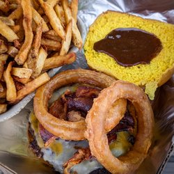 Chewy Burger, topped with bacon, cheese, onion rings, and BBQ sauce, on a corn bun