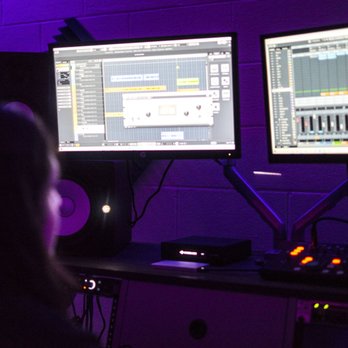 Full Range Studio B - Engineer recording my niece! - A person is seated at a desk with two monitors showing music production software, surrounded by audio equipment in a dimly lit studio. - Recording & Rehearsal Studios Near Me - Montclair, California
