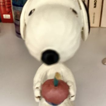 Enesco - My Jim Shore Design Snoopy from Enesco. Posted with review 01/02/24 - A Snoopy figurine with a hollow head and body, holding a red heart-shaped object with a small candle on top, placed on a shelf. - Gift Shops Near Me - Itasca, Illinois
