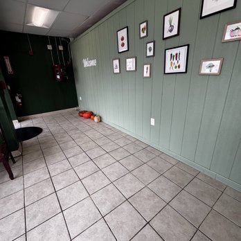 Thai Accent - Front entrance - The image shows an indoor space with beige tiled flooring and a green paneled wall decorated with various framed botanical illustrations. The wall has a 'Welcome' sign, and pumpkins are arranged on the floor near the corner. The ceiling has a fluorescent light fixture, and there are fire safety devices mounted on the dark green wall in the background. - Thai Near Me - West Warwick, Rhode Island