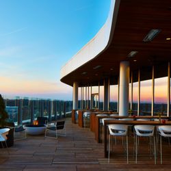VASO - Sunset casts a warm glow on VASO's rooftop patio, featuring modern seating, fire pits, and panoramic views behind glass railings.