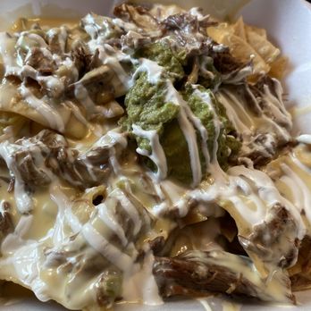 Mamacitas - Nachos - A foam takeout container holds nachos with shredded beef, guacamole, and drizzles of white and brown sauces, served with a black plastic fork. - Mexican Near Me - Clovis, New Mexico
