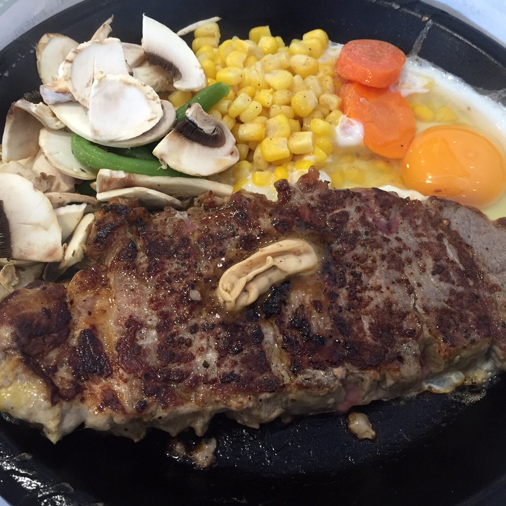 Big porterhouse stake with mushrooms & egg on stone grill.