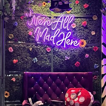 Alice In Appalachia - a purple couch with a pink pillow and a neon sign that says never all mad here - Cocktail Bars Near Me - Knoxville, Tennessee Alice In Appalachia - a purple couch with a pink pillow and a neon sign that says never all mad here - Cocktail Bars Near Me - Knoxville, Tennessee