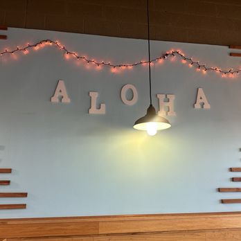 Poke Wave - Wall mural - Wall decorated with string lights, a hanging lamp, and large white letters spelling "ALOHA" in a space with wooden accents. - Poke Near Me - Tempe, Arizona