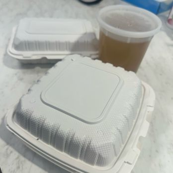 Pho 75 - Two white, sealed takeout containers and a cup of iced coffee with a lid are placed on a marble table, with tissue and other items in the background. - Vietnamese Near Me - Aurora, Colorado