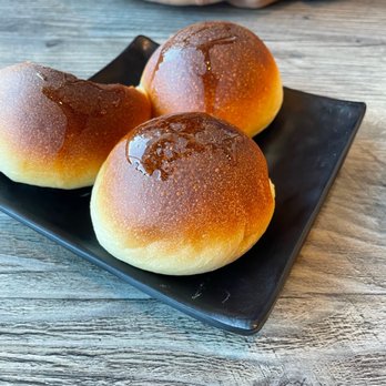 IT DIMSUM - Three steamed buns with glossy, glazed tops are arranged on a black square plate on a wooden table. - Dim Sum Near Me - Albuquerque, New Mexico