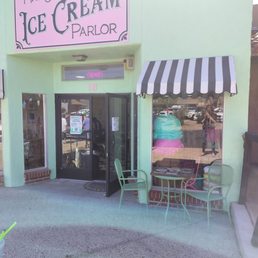 Mrs. Sprinkles Ice Cream Parlor has a pastel green facade, a pink sign, and a striped awning. There are outdoor chairs and a table near the entrance.