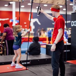 Gymnastics coach helping a young gymnast with a junior ninja training course