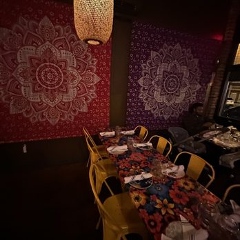 Kai Yang - A restaurant interior features a long table with floral tablecloths, yellow chairs, and decorative mandala wall art in red and purple backgrounds. - Thai Near Me - Montclair, New Jersey