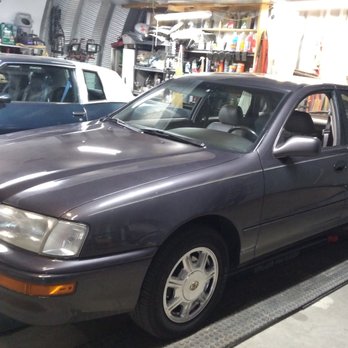 R & Z Service - A dark gray vintage coupe car is parked inside a garage, with a blue classic car visible in the background and various tools and supplies on shelves. - Auto Repair Near Me - Albuquerque, New Mexico