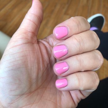 Epic Nail Spa - Regular non-gel mani - The image features a person's left hand with nails painted in a glossy pink color. The hand is positioned with the palm facing slightly upward, and the fingers are curled inward. The background shows a wooden floor, and part of a person's leg and shoe are visible in the upper right corner. The nails are well-manicured and shiny. - Nail Salons Near Me - Mattituck, New York
