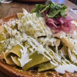Let's go. Green enchiladas - Plate of green enchiladas with cheese, sour cream, pickled red onions, and cilantro, served in a rustic bowl at a restaurant.