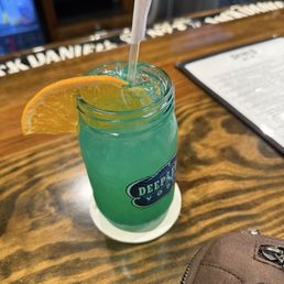 A blue-green cocktail with an orange wedge garnish and a straw is placed on a bar counter at a Nashville-themed venue.