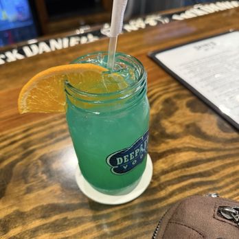 Daisy's Nashville Lounge - A blue-green cocktail with an orange wedge garnish and a straw is placed on a bar counter at a Nashville-themed venue. - Lounges Near Me - Patchogue, New York