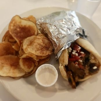 Threefold Cafe - Chicken shawarma - A white plate contains a serving of potato chips, a beef taco wrapped partially in aluminum foil with visible toppings like diced tomatoes and cheese, and a small plastic container of sauce. The setting appears to be a casual dining environment, possibly a restaurant or cafe. - Coffee & Tea Near Me - Chestnut Ridge, New York