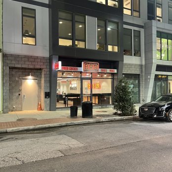 BRD - Storefront - BRD, a fried chicken restaurant, has a lit sign and large windows showing the interior, located on a city street with parked cars and sidewalk. - Chicken Shop Near Me - Baltimore, Maryland