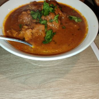 Curry Corner - Chicken tikka masala - A white bowl filled with chicken tikka masala, topped with cilantro, sits on a wooden table with a spoon inside. - Pakistani Near Me - Tempe, Arizona