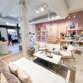 Uncommon James - A boutique store interior featuring seating, shelves with decor, and a pink accent wall with a logo. The space has modern decor and lighting. - Accessories Near Me - Chicago, Illinois