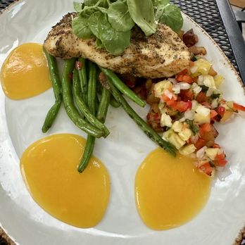 The James - Grilled Halibut - A dish with grilled fish, green beans, yellow fruit compote, and a vegetable medley is presented on a white plate, garnished with greens. - Wine Bars Near Me - Geneva, Illinois