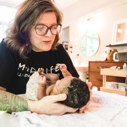 Mothership Midwifery - Connecting with a sweet baby during the newborn exam. Mom is having a snack snuggled in bed watching the exam right at her feet.