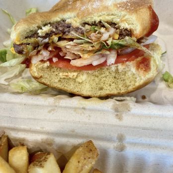 Kaliburger - Impossible Vegan burger - A close-up of a partially eaten vegan burger featuring a plant-based patty, shredded lettuce, and sliced tomato in a bun. The burger is placed in a disposable container with some shredded lettuce and ketchup visible. French fries are partially visible at the bottom of the image, served alongside the burger. The setting appears to be a casual takeout meal. - Burgers Near Me - St. Augustine, Florida