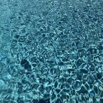 Vineyard Pools - Tahoe Pebble deep end of pool - The image depicts the deep end of a swimming pool with clear water, showing ripples and reflections on the surface. The water appears clean and blue, with light reflections creating a pattern of waves and distortions. The pool's bottom is visible through the water, indicating good water clarity. - Landscaping Near Me - Clovis, California
