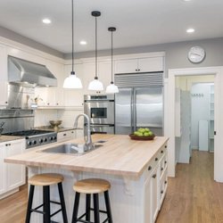 Modern white kitchen with shaker cabinets, stainless steel appliances, wood island countertop, pendant lights, recessed light...