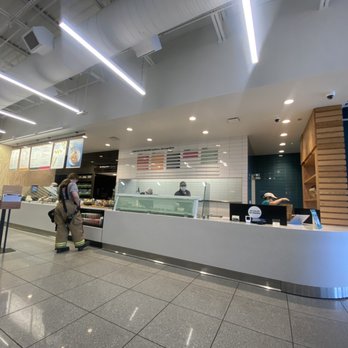 Chopt Creative Salad - The cleanest and most friendliest staff!! - A contemporary food service counter in a shopping mall features a white curved design, with customers and staff visible, and menu boards overhead. - Salad Near Me - Fairfax, Virginia