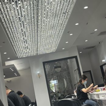AVA Nail Bar - A nail salon interior featuring a large, ornate crystal chandelier, clients seated in black chairs, and a technician working on a client while wearing a face mask. - Nail Salons Near Me - Schaumburg, Illinois
