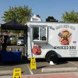 Home for happy carnivores. - A white food truck called Mighty Mike's Meats offering smoked BBQ, with cartoon graphics, parked in a lot with people and signs.