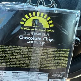 A clear plastic bag contains a chocolate chip muffin top from The Human Bean, featuring a yellow sun logo and text about making your day brighter.