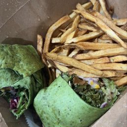 jerk chicken Spinach Jerk Chicken ($12 Meal) - Spinach jerk chicken wrap with friesSpinach Jerk chicken Combo - A takeout box contains a burrito wrapped in a green tortilla, filled with salad ingredients such as lettuce and onions. Next to the burrito, there is a serving of French fries. The box appears to be made of brown paperboard, and the fries are golden-brown and crispy. The image suggests a meal from a restaurant offering casual, fast-food-style dishes.