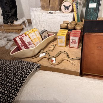 Luna and Luz - (6/13/2023) - A table features small product boxes, jars, notebooks, and a snake figurine, with a background of foam and decorative items. - Jewelry Near Me - Albuquerque, New Mexico