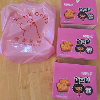 Snack Oasis - Three pink boxes of fish tofu snacks with cartoon character illustrations and a pink plastic bag from Snack Oasis are placed on a wooden surface. - Convenience Stores Near Me - Chicago, Illinois