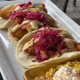 Fish Tacos - Three fish tacos with breaded fish, shredded red cabbage, and chopped vegetables, topped with sauce, served on a white tray.