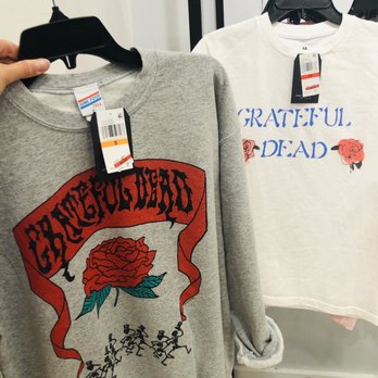 Macy's - GD Merch...at Macy's?! - Two graphic T-shirts featuring band names and floral artwork are shown on hangers in a retail store. One is gray with 'GRATEFUL DEAD' and a rose, the other is white with similar text and design. - Department Stores Near Me - Phoenix, Arizona