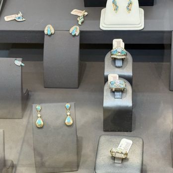 Feathers Galleria - The image features a jewelry display with various rings and earrings, primarily set with opal stones, arranged on gray stands of different heights. The display is in a retail environment, with some jewelry pieces placed on small, rectangular platforms and others directly on stands. The jewelry includes rings with large opal stones and earrings with matching opal accents, all presented in a neat and organized manner. - Jewelry Near Me - Santa Fe, New Mexico