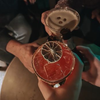 Common Tiger - Hibiscus Margarita and Espresso Martini - Three individuals are holding different cocktails with garnishes, including a dried citrus slice and a cherry, in a low-light environment. - Speakeasies Near Me - Mission, Kansas