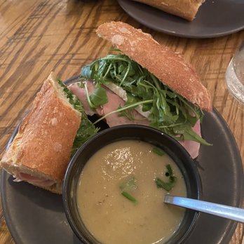 Tilman's - Ham baguette & spice leek soup.  Yum - A sandwich with ham, arugula, and toasted bread slices is served with a bowl of creamy soup on a black plate at a restaurant. - Wine Bars Near Me - Charlottesville, Virginia