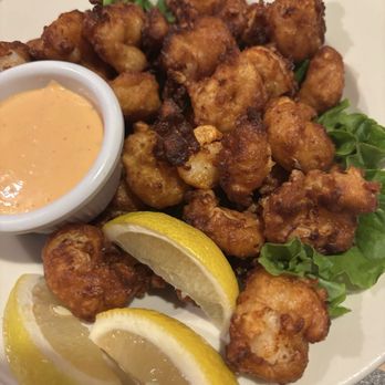The Rye Roadhouse - Plate of fried chicken bites with lemon wedges, a dipping sauce, and some greens, presented on a white dish. - Cajun/Creole Near Me - Rye, New York
