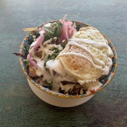Carnitas breakfast bowl with 2 eggs over easy pickled red onion crema and cilantro on top of home potatoes aka casa potatoes.