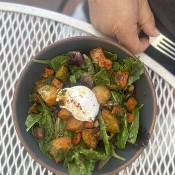 Coronet Cafe - Breakfast Bowl - A bowl of mixed greens topped with roasted potatoes, vegetables, and a poached egg, placed on a metal outdoor table. - Cafes Near Me - Tucson, Arizona